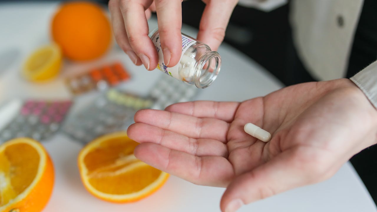 A person holding supplement capsules with a glass of water, morning wellness routine