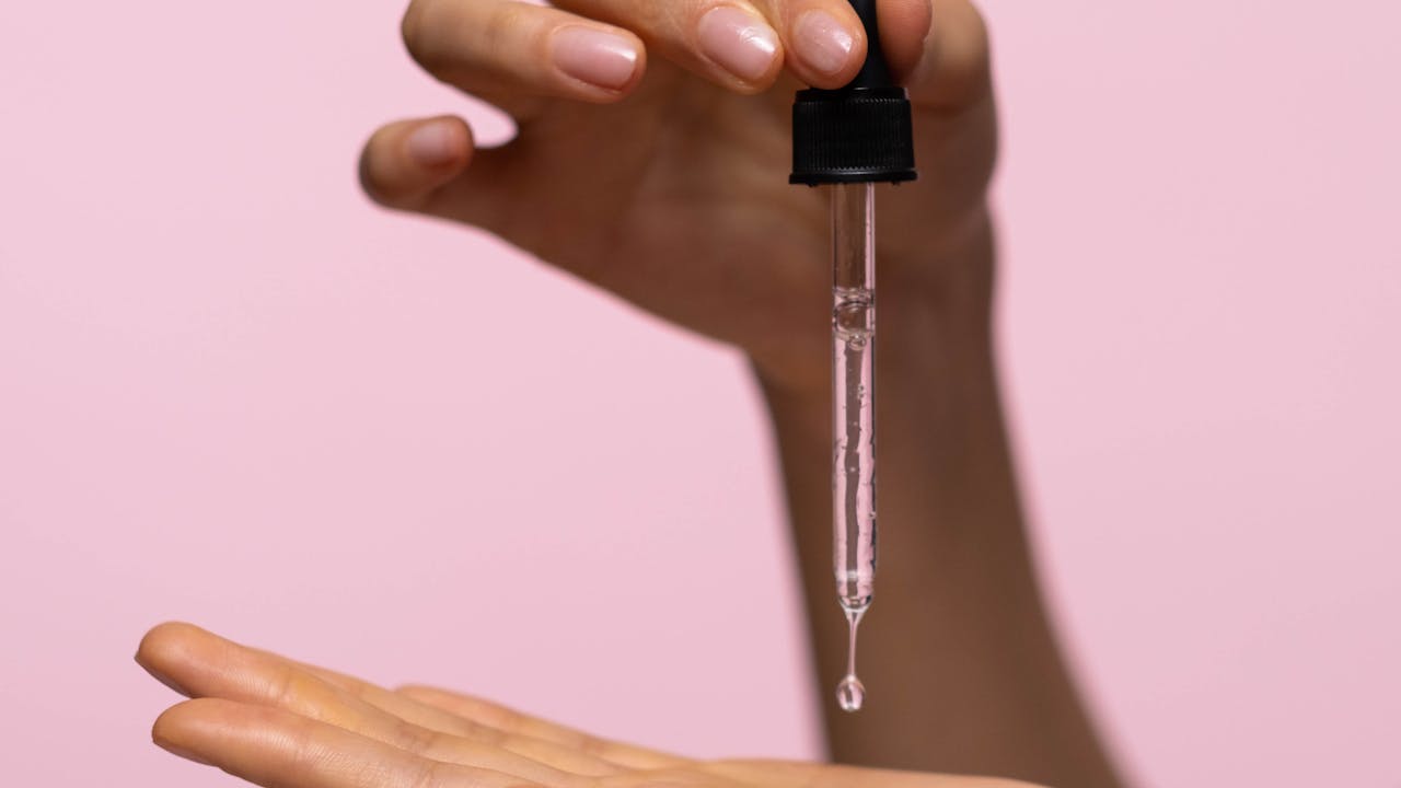 Person holding a glass dropper carefully measuring liquid supplement drops