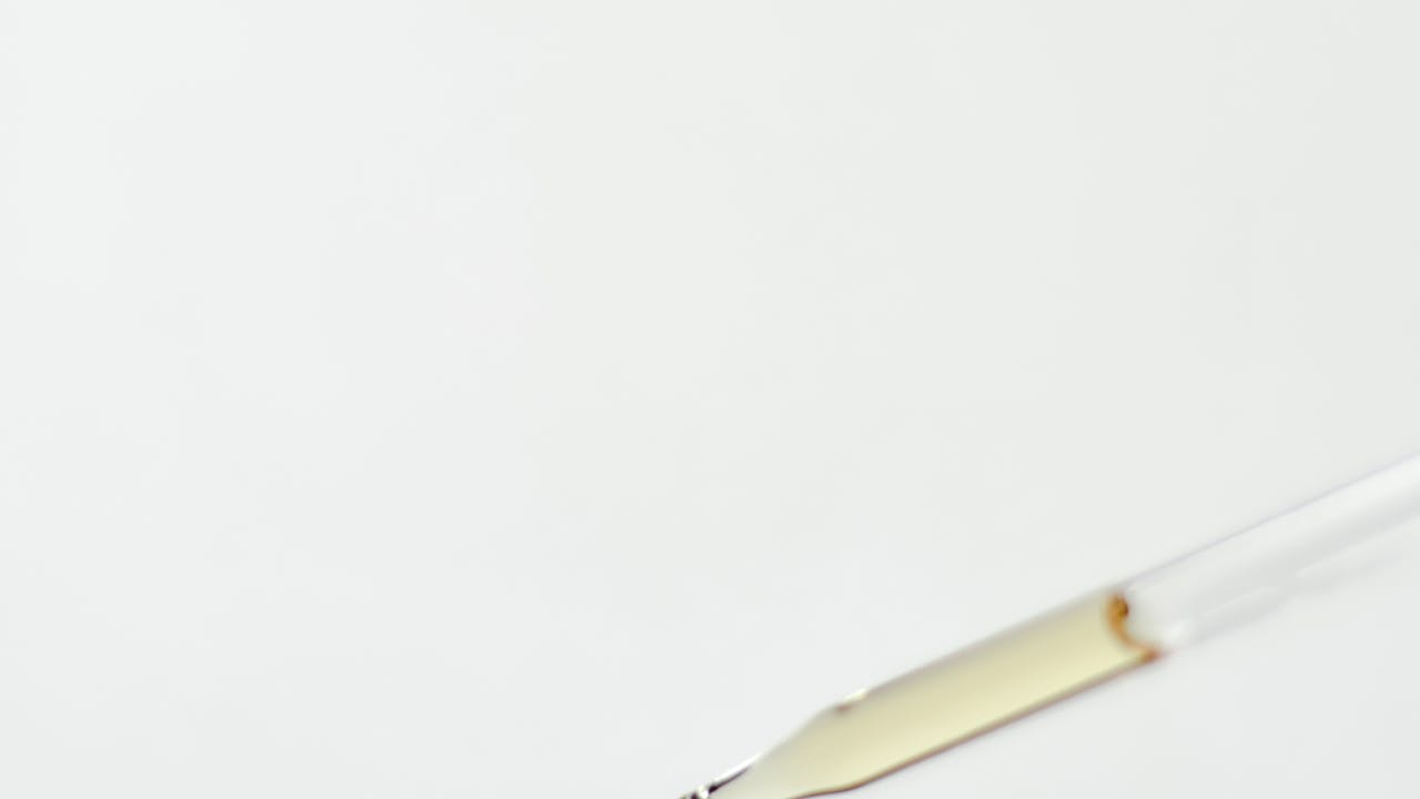 Medicine dropper with a precise drop of liquid suspended above a glass bottle