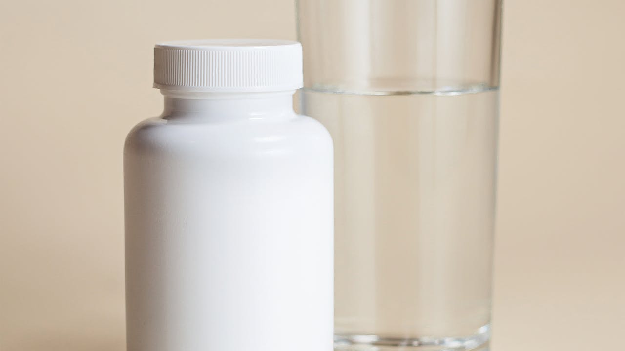 A clear glass of water next to a supplement bottle on a clean countertop